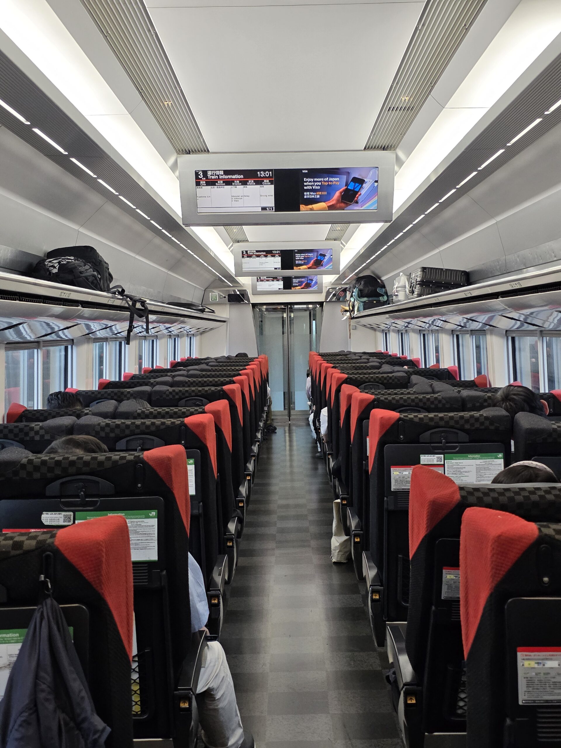 Interior do Narita Express a caminho do centro de Tóquio, com passageiros sentados e ecrãs informativos — transporte rápido desde o aeroporto de Narita