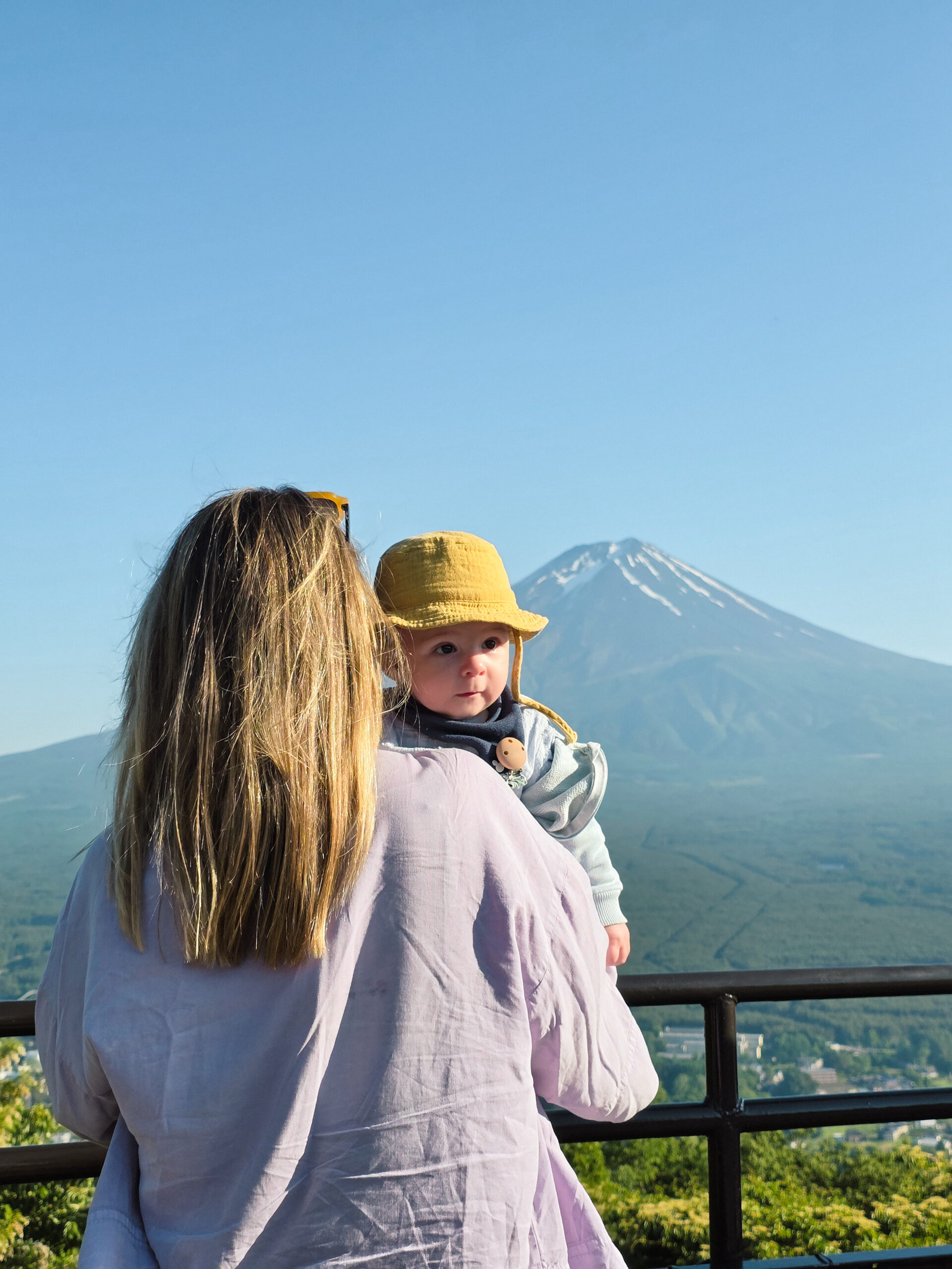 Mãe com bebé ao colo a admirar o Monte Fuji num dia claro, durante uma viagem ao Japão